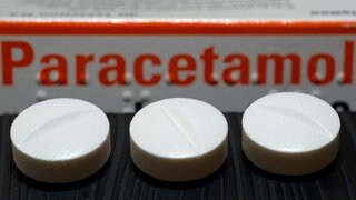 Vor einer Arzneiverpackung liegen Tabletten, die den Wirkstoff Paracetamol enthalten.