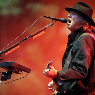 Neil Young auf der Bühne singend am Mirko mit Gitarre in der Hand