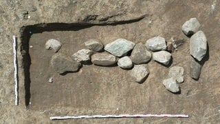 Einige Steine und Massstäbe sind in einer Grube zu sehen.