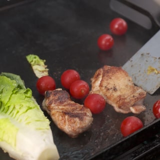 Salat, Hähnchen und Cocktailtomaten liegen auf einem Grill