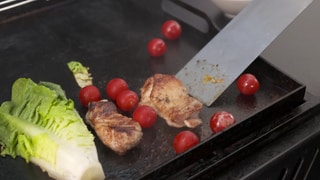 Salat, Hähnchen und Cocktailtomaten liegen auf einem Grill