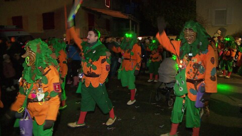Verkleidete Menschen ziehen in einem bunten Fasnachtsumzug durch das Dorf, umringt von jubelnden Zuschauern.