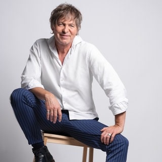 Sänger Peter Freudenthaler sitzt auf einem Stuhl und schaut in die Kamera.