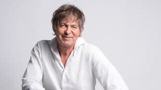 Sänger Peter Freudenthaler sitzt auf einem Stuhl und schaut in die Kamera.