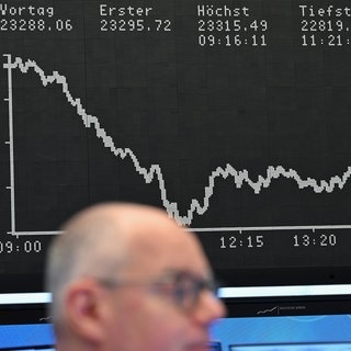 Ein Börsenhändler auf dem Parkett der Frankfurter Wertpapierbörse vor der Anzeigetafel mit der DAX-Kurve