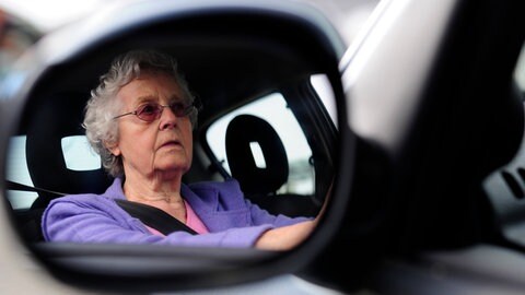 Seniorin sitzt hinterm Steuer und fährt Auto mit Führerschein.