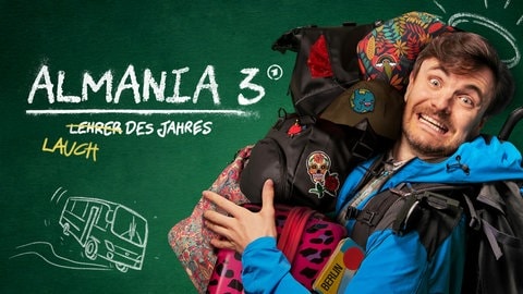 Ein Mann mit überforderter Miene trägt mehrere bunte Taschen und Rucksäcke vor einer grünen Tafel, auf der „Almania 3“ und skizzierte Zeichnungen zu sehen sind.