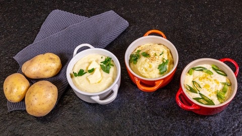Rezept für Kartoffelpüree: Drei kleine Töpfe in grau, orange, rot stehen im Halbkreis nebeneinander und sind gefüllt mit Variationen von Kartoffelpüree.