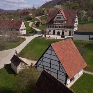 Mehrere Fachwerkhäuser stehen im Freilichtmuseum Beuren. Drum herum erstrecken sich grüne Hügel.