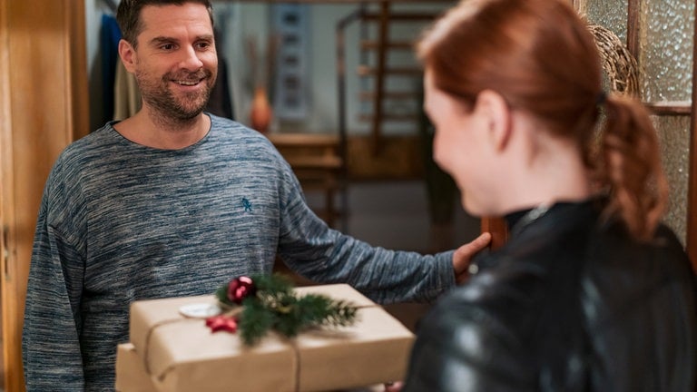 Andreas (Ralph Gassmann) hat die Haustür geöffnet, davor steht Lissy (Elinor Eidt) mit Weihnachtsgeschenken