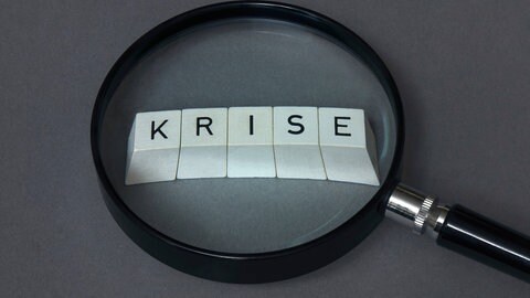 Unter einer Lupe wird das Wort "Krise" vergrößert. Sinkt die Zufriedenheit in einer Beziehung, so die neue Studie, wird ein Ende vorhersehbar.