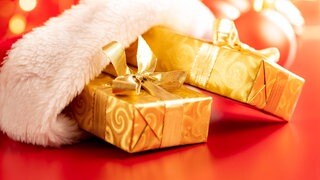 Wundervolles Winterwissen - der SWR1 Adventskalender: Warum packen wir Geschenke ein? Das Bild zeigt Geschenke, die in goldenes Geschenkpapier gewickelt und mit goldenen Schleifen versehen sind. Sie stecken halb in eine roten Nikloaus-Mütze mit weißem Fellbesatz.
