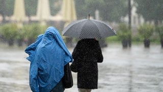 Ein Mensch schützt sich mit einer Jacke vor dem Regen, eine andere Person hat einen Schirm.