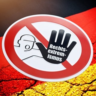 Warnschild mit der Aufschrift "Rechtsextremismus" auf einer Deutschlandfahne mit Rissen: Manche Bundesländer wollen Beamte stärker auf ihre politische Gesinnung überprüfen. In den 1970ern gab es den Radikalenerlass. Kehren Berufsverbote nun zurück?