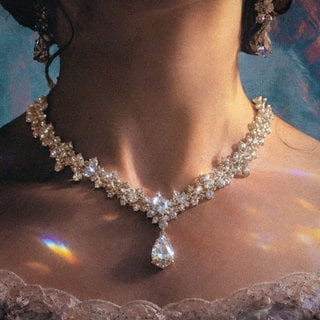 Nahaufnahme einer Person in eleganter historischer Kleidung, die ein aufwendig gearbeitetes Diamantenhalsband mit funkelnden Schmucksteinen und tropfenförmigem Anhänger trägt. Lichtreflexe verleihen der Szene eine glamouröse und luxuriöse Atmosphäre. 