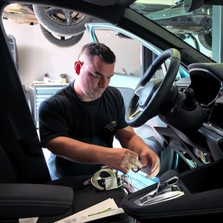 Kevon Urban aus Lichtenwald baut Autos behindertengerecht um. Er kniet vor der geöffneten Fahrertür und schraubt an der Elektronik.