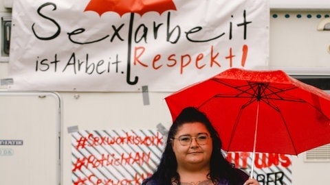 Eine Sexarbeiterin mit rotem Regenschirm in der Hand demonstriet am 22. Juni 2021 vor dem Kölner Dom vor einem Schild mit der Aufschrift: "Sexarbeit ist Arbeit. Respekt!"