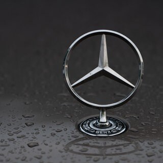 Regentropfen sind auf einem Mercedes-Stern auf einem Fahrzeug zu sehen (Symbolbild).