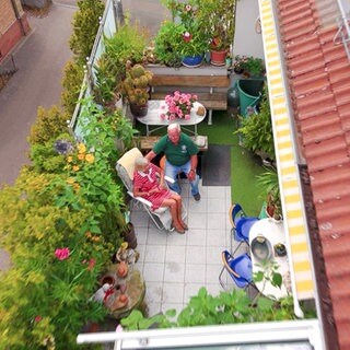 Ein älteres Paar sitzt auf einem großen Balkon mit vielen Pflanzen.