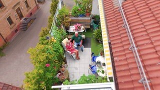 Ein älteres Paar sitzt auf einem großen Balkon mit vielen Pflanzen.