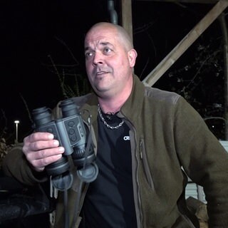 Dennis ist Jäger. Er trägt eine khakifarbene Jacke und hält ein Fernglas in der Hand.