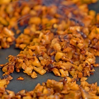 In einer Pfanne sind kleingehackte Pilze und Walnüsse, aus denen veganes Hack gemacht wird. Eine Alternative zu Fleisch für Bolognese und andere Saucen.