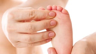 Mutter massiert Fuß und Zehen ihres Säuglings mit den Fingern: Evolutionstechnisch sind Finger- und Zehennägel ein Überbleibsel von entfernten Vorfahren, die noch Krallen zum Klettern hatten. 