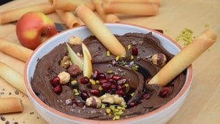 Schokoladen-Hummus in einer Schale garniert mit Nüssen, Granatapfelkernen und Pistazien.