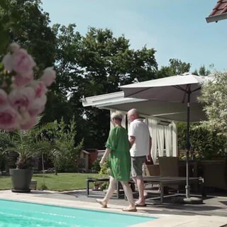 Ein Ehepaar läuft in einem idyllischen Garten mit Terrasse Pool und Rosen