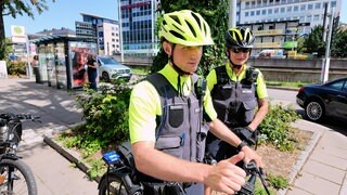 Ein Fahrradpolizist und eine Fahrradpolizistin sind in Stuttgart unterwegs. Sie stehen an einer Straße.