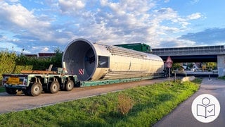 Ein Schwer·transporter mit einem großen Metall·behälter steht vor einer Brücke. Der Schwer·transporter ist bei Heilbronn unter der Brücke stecken geblieben. Rechts das SWR Logo für Leichte Sprache.
