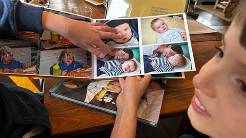 Mattia zeigt mit seinem Finger auf ein Foto von sich als lachendes Baby, daneben liegt seine Mutter. Weil er durch seinen Gendefekt weniger Muskulatur hat, brauchte es lange bis er das erste mal richtig gelächelt hat.
