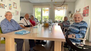Die Bewohnerinnen und Bewohner der WG für Menschen mit Demenz in Alzey sitzen gemeinsam an einem langen Tisch.