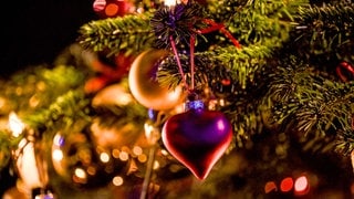 Ein Herzanhänger hängt an einem geschmückten Weihnachtsbaum. 