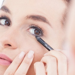 Eine junge Frau benutzt einen Kajalstift am unteren Wimpernkranz. Symbolfoto.