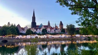 Das Donaufest 2026 bei Abendstimmung - volle Ufer, Lichterketten und im Hintergrund das Ulmer Münster.