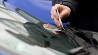 Jemand klemmt einen Strafzettel hinter den Scheibenwischer eines Autos (Symbolbild). In Tübingen haben Unbekannte gefälschte Strafzettel verteilt. 