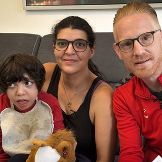 Mutter, Vater und Kind mit Behinderung sitzen auf einem Sofa