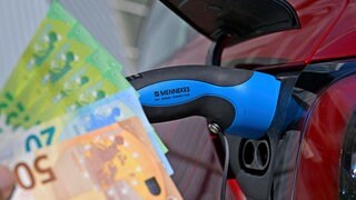 Öffentliche Ladesäule für E-Autos an einem Parkplatz, Ein Tesla Model 3 lädt gerade seinen Akku an der Stromtankstelle voll, der Stecker steckt im Ladeanschluss des Autos. Gestiegene Strompreise machen den Bürgern zu schaffen.
