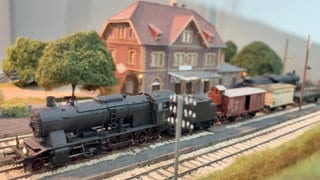 Eine Modell-Lokomotive der Brenztalbahn steht auf den Gleisen. Im Hintergrund ist eine Miniatur-Nachbildung eines Backsteinhauses zu sehen, dass den Sontheimer Bahnhof darstellen soll.