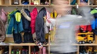 Ein Kind flitzt durch die Garderobe einer Kita (Symbolbild): Ab August gibt es in Rheinland-Pfalz eine neue Ausbildung. Sozialpädagogische Assistenten sollen künftig neben Erziehern in Kitas arbeiten und diese unterstützen.