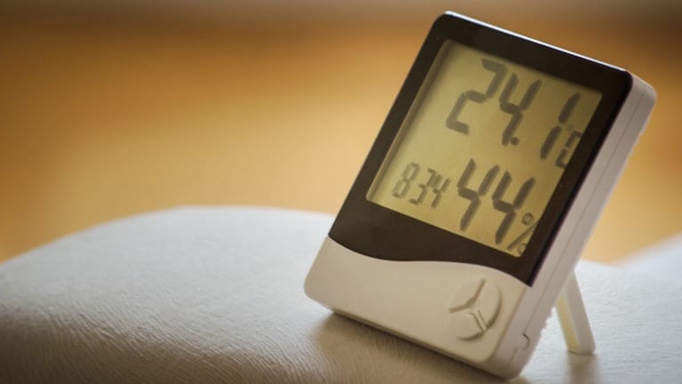 Ein Hygrometer steht auf einem Sofa und zeigt die Wärme und Luftfeuchtigkeit an