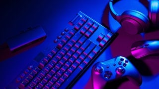Eine Computertastatur, eine Maus und ein Joystick liegen auf einem schwarzem Hintergrund.