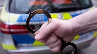 Ein Polizist hält Handschellen vor einem Einsatzfahrzeug hoch.