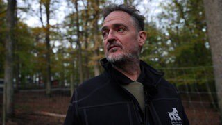 Rainer Kniele transportiert Wildtiere. Er steht in einem Wildtiergehege im Wald.