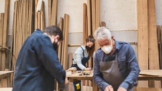 Ein Handwerker Team mit Mundschutz wegen Covid-19 arbeitet in einer TischlereiWerkstatt.