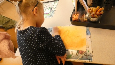 Malprojekt 2024 der Elternbegleitung Schweinfurt: Ein Kind malt ein Blatt Papier gelb an. 