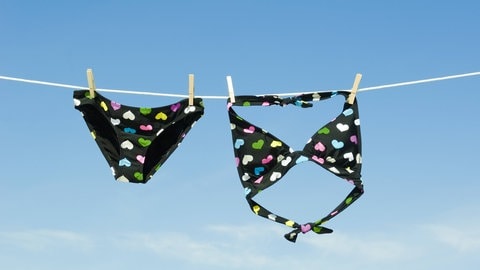 Ein schwarzer Bikini mit Herzchen hängt an einer Wäscheleine