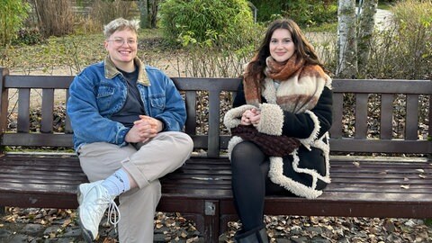 Die beiden Careleaverinnen Jamie (links) und Jette (rechts) sitzen auf einer Bank