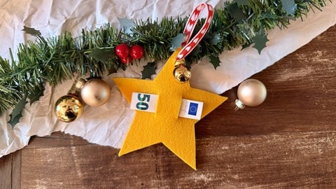 In der Mitte eines gelben Filzsterns ist durch zwei Schlitze ein eingerollter Geldschein gesteckt. Eine schöne Bastelidee, um an Weihnachten Geld zu verschenken.